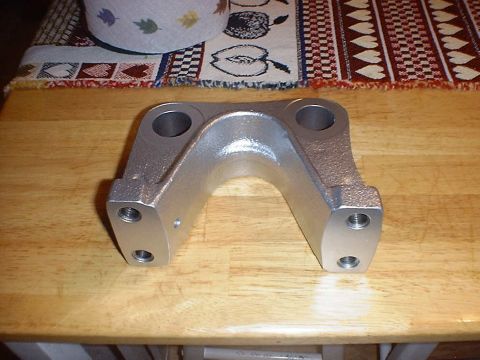 1988 Ford Bronco - A cast, arch-shaped suspension bracket with two large machined bores on top and four tapped bolt holes in its flat side pads, sitting on a…