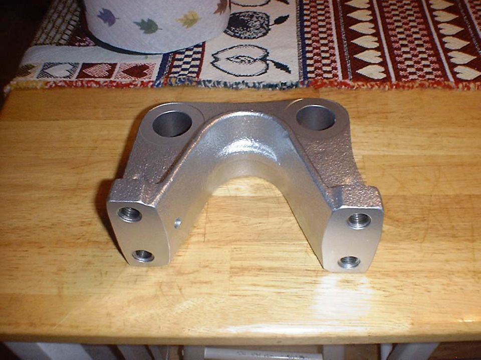 Cast arched suspension bracket with two machined bores and tapped side pads on a wood table