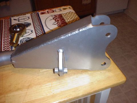 1988 Ford Bronco - Silver-painted fabricated radius arm resting on a butcher-block kitchen table, showing the boxed plate axle end with three bolt holes, a we…