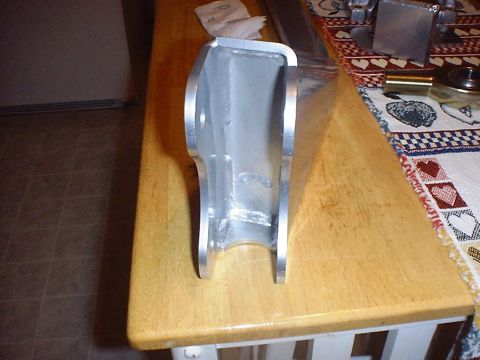 1988 Ford Bronco - A bare aluminum fabricated bracket with a rounded top edge, notched U-shaped bottom cutout and visible weld beads sits on a butcher-block k…