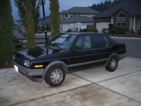 1987 Volkswagen Golf - A black sedan sits in a driveway in front of houses and trees.