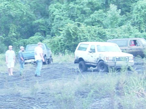 1989 Ford Bronco - Several off-road vehicles are seen in a muddy area with trees in the background.