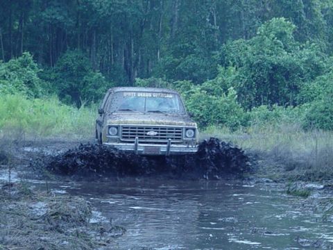 1989 Ford Bronco - A tan pickup truck navigates a muddy obstacle course, splashing water and mud.
