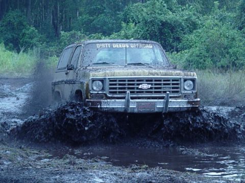 1989 Ford Bronco - Mud splatters as a Chevrolet K5 Blazer navigates a muddy trail, with "DIRTY DEEDS OFFROAD" visible on the windshield.