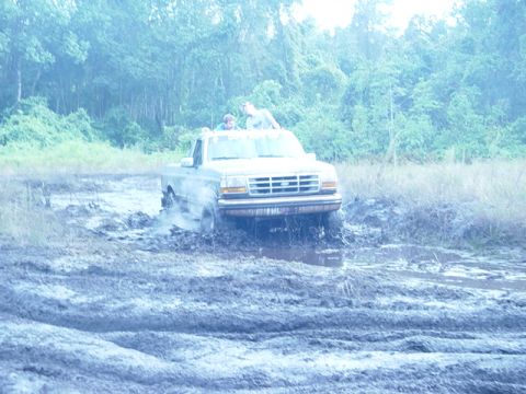 1989 Ford Bronco - A Ford pickup truck navigates a muddy terrain with two occupants visible inside the cab.