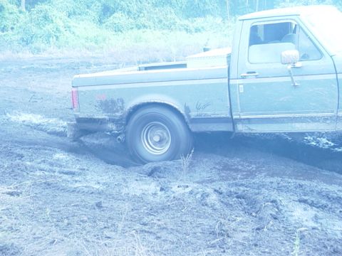 1989 Ford Bronco - A Ford F-Series truck is stuck in the mud, with its rear wheel spinning.