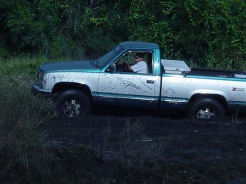 1989 Ford Bronco - This pickup truck appears to be stuck in a muddy area with trees in the background.