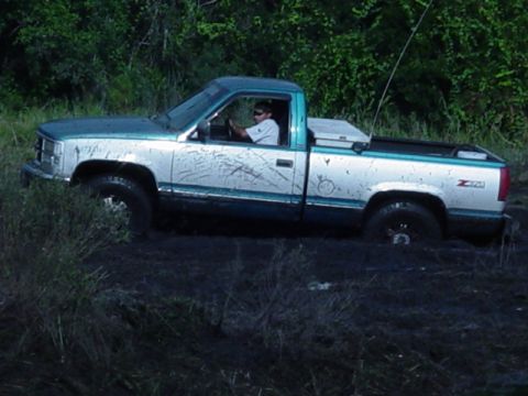 1989 Ford Bronco - A driver navigates a two-tone Chevrolet C/K pickup truck through a muddy off-road course.