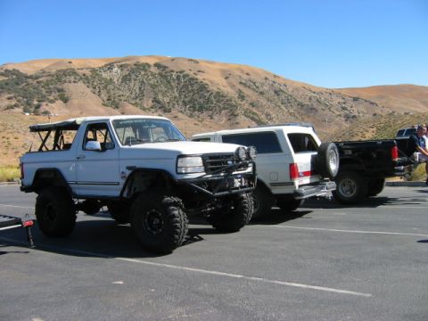 1985 Ford Bronco - Three trucks are parked in a lot with a hilly landscape in the background.