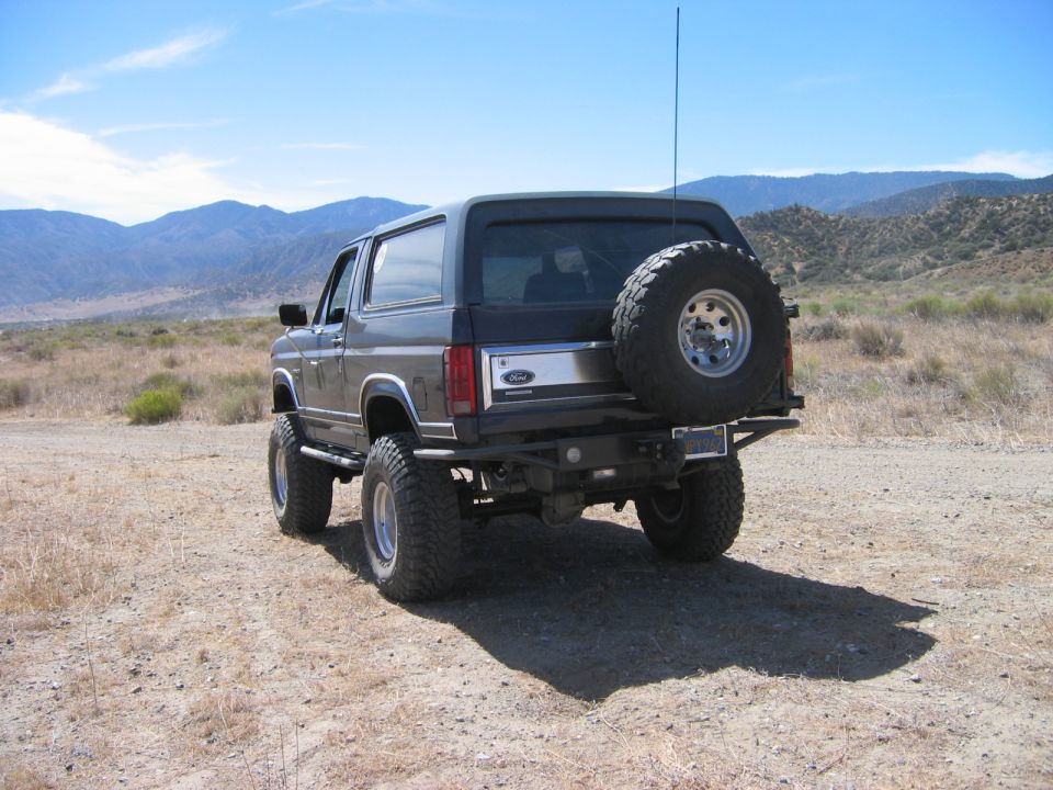 Lifted gray and black Ford Bronco SUV, rear view, spare tire mounted, in desert.