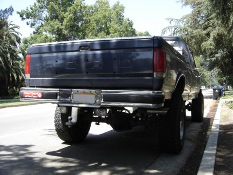 1987 Ford F-250 - Rear view of a dark blue 1987 Ford F-250 pickup truck a lifted suspension and prominent Ford badging on the tailgate.