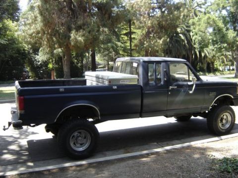 1987 Ford F-250 - This lifted, crew cab Ford pickup truck is parked on a street with trees in the background.