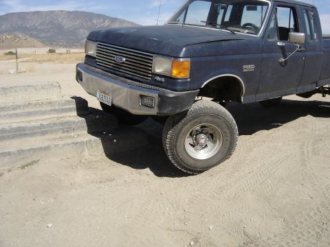 1987 Ford F-250 - This 1987 Ford F-250 pickup truck is shown in a three-quarter front view, a lifted suspension and dark blue paint.