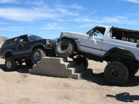 1985 Ford Bronco - Two Ford Broncos tackle a challenging off-road course, demonstrating their capabilities on uneven terrain.