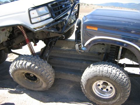1985 Ford Bronco - Two heavily modified Ford trucks are positioned on a set of stairs, demonstrating their off-road capabilities.