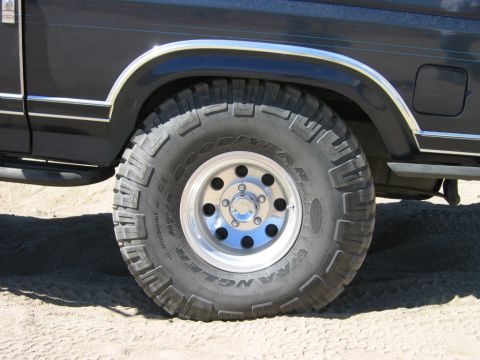 1985 Ford Bronco - Close-up view of a dark SUV's side, highlighting its large Goodyear Wrangler tire and chrome fender trim.