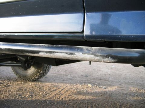 1985 Ford Bronco - Close-up side view of a dark SUV's running board showing wear and tear.