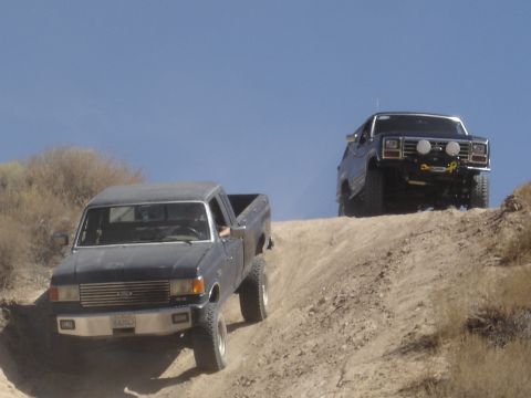 1987 Ford F-250 - Two pickup trucks, including a 1987 Ford F-250, navigate a steep dirt incline under a clear blue sky.