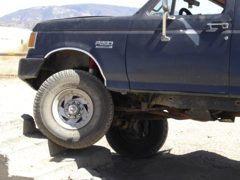 1987 Ford F-250 - A dark blue Ford F-250 truck is shown with its front wheel on a rock, highlighting its off-road capability.