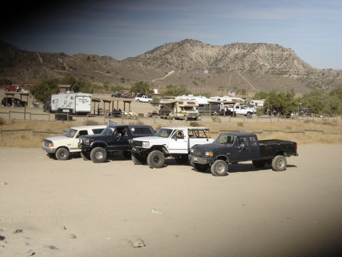 1987 Ford F-250 - Several lifted trucks and RVs are parked at a campsite in a desert landscape.