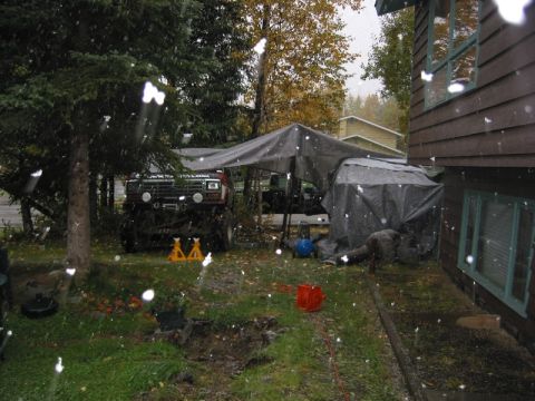 1985 Ford Bronco - A modified off-road vehicle sits under a tarp in a yard during a snowfall.