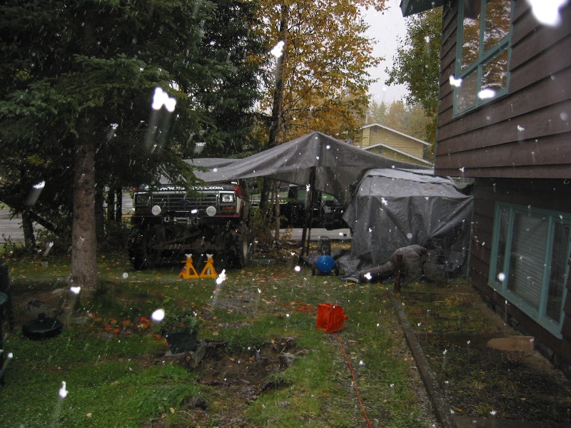 Lifted dark Ford truck under a tarp shelter in a snowy backyard with jack stands and tools