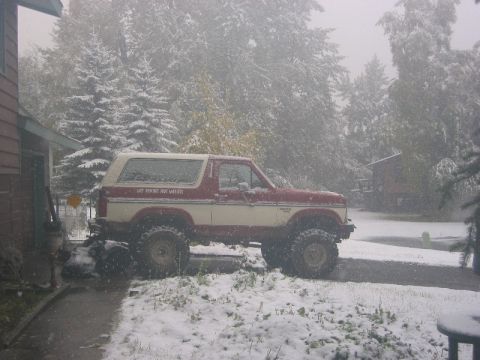 1985 Ford Bronco - A red and white Ford Bronco with a lifted suspension sits in the snow, displaying the 'Last Frontier Four Wheelers' text on its side.