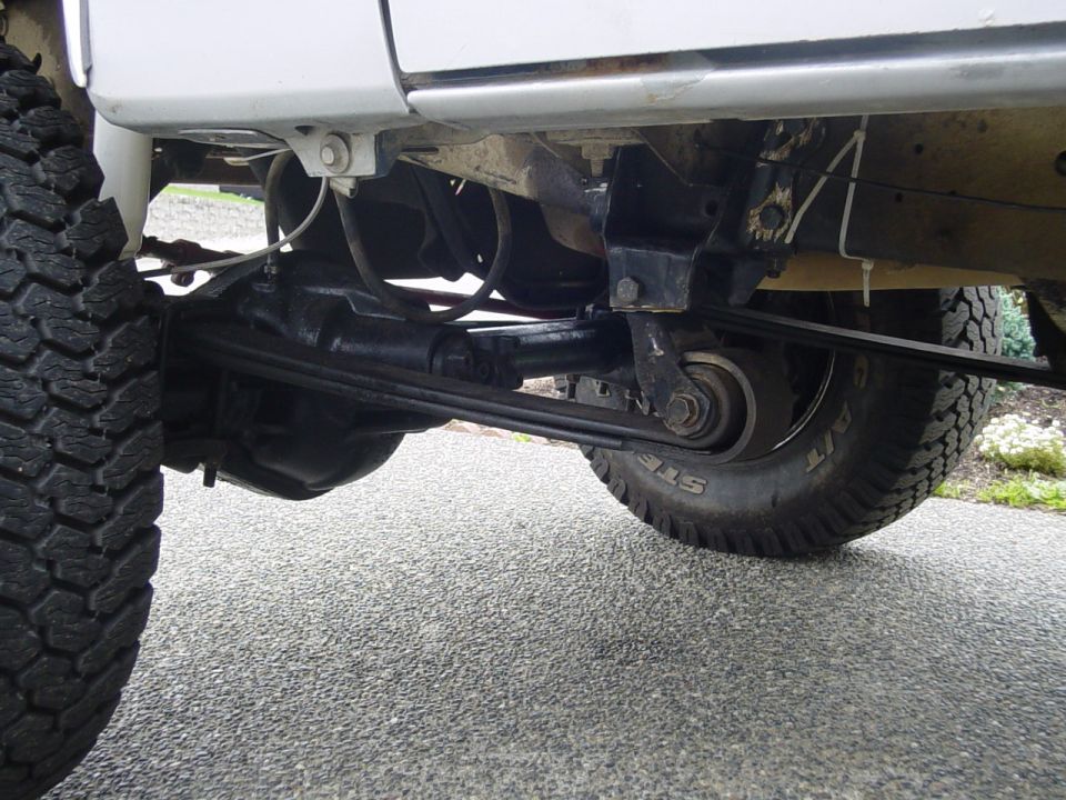 Undercarriage of lifted truck showing front axle, steering linkage, and mud-terrain tire