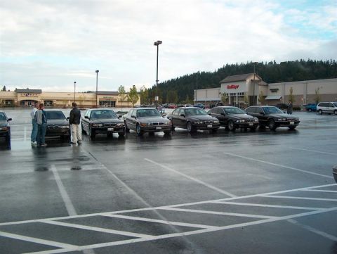 1999 BMW 7 Series - A group of BMWs are parked in a lot under a cloudy sky, with a grocery store in the background.