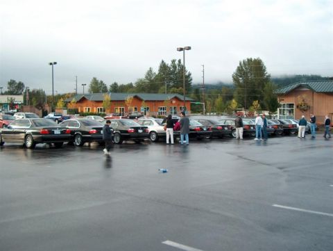1999 BMW 7 Series - Several 1999 BMW 7 Series sedans are parked in a lot, with people standing around them.