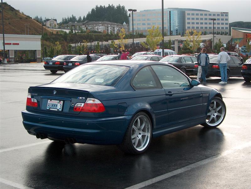 Rear 3/4 view of teal BMW E46 coupe with silver wheels in wet parking lot