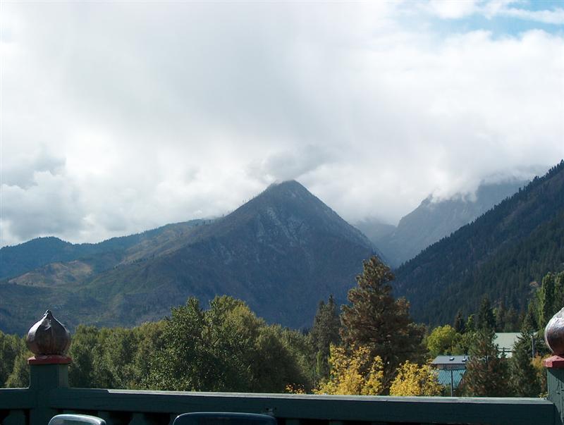 Cloud-topped mountain peak and forested slopes seen over a railing