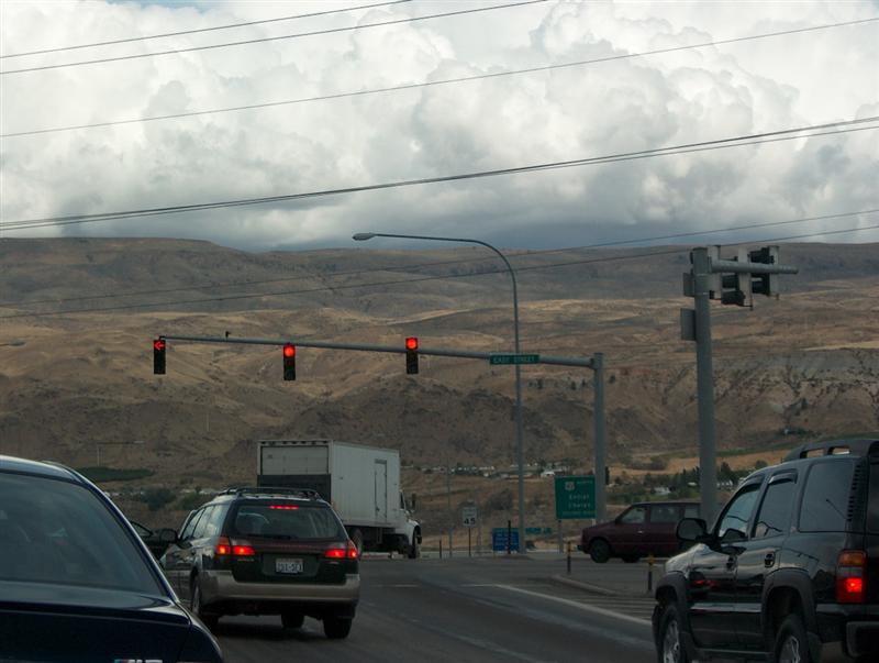 Traffic at a red light on a highway with dry brown hills and cloudy sky in distance