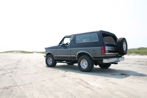 1993 Ford Bronco - A Ford Bronco is parked on a sandy beach with dunes in the background.