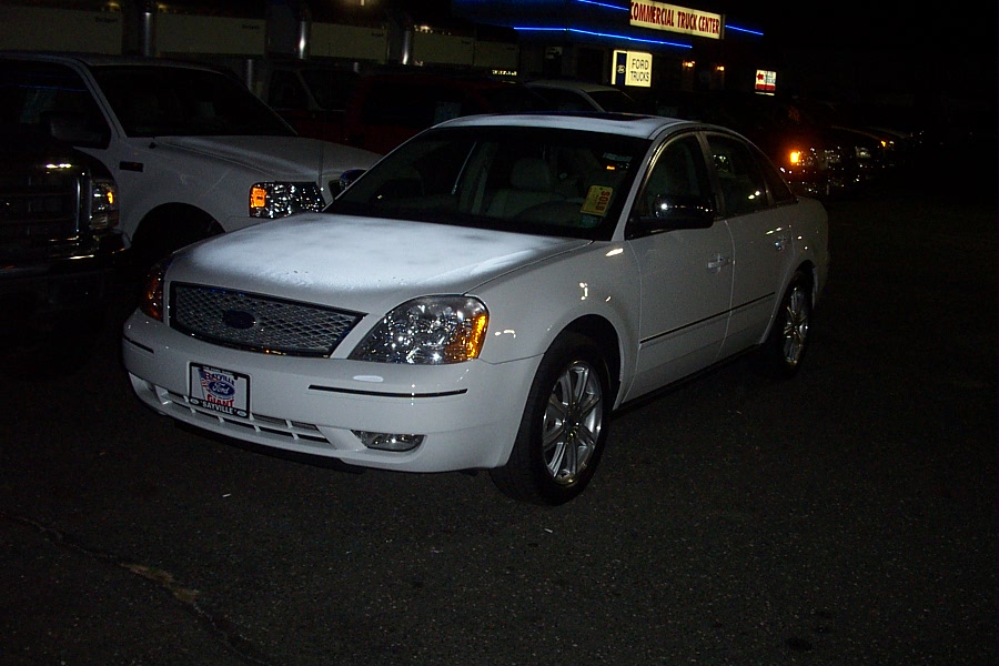 White sedan with chrome grille and headlights, parked at night. Another white truck is visible to the left