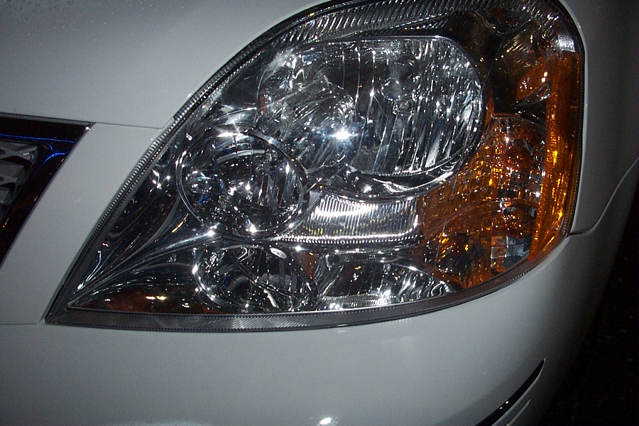 Close-up of a white car's headlight assembly with chrome accents and an amber turn signal