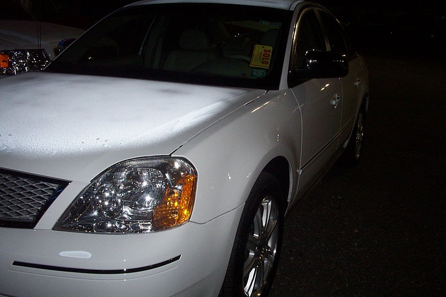 White sedan with chrome wheels and a yellow 'SOLD' tag on the windshield