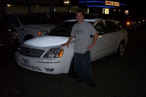 1993 Ford Taurus - A man poses with a white sedan outside a commercial truck center at night.