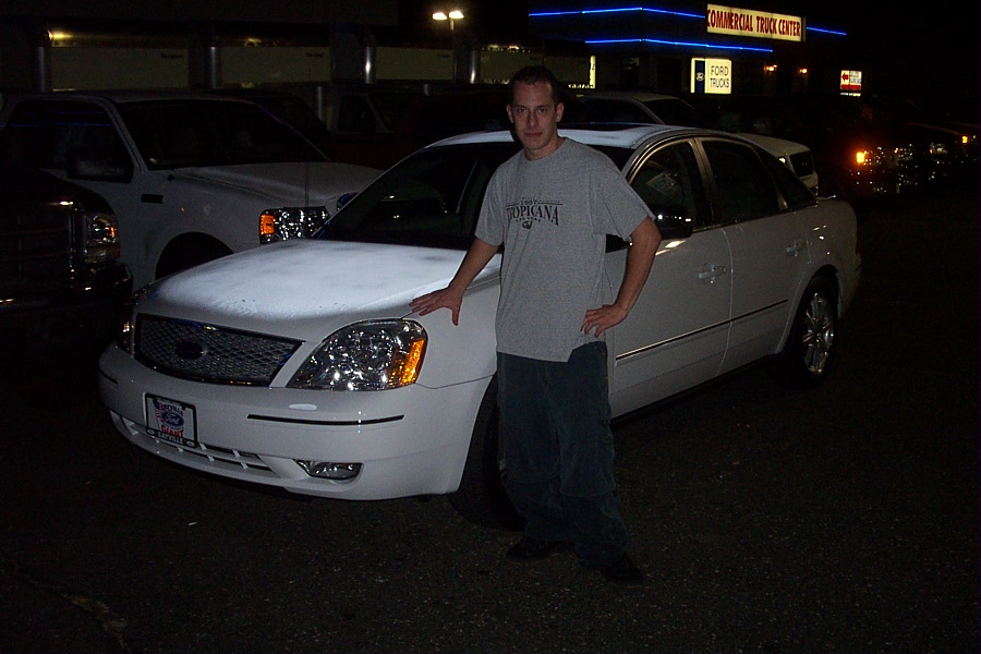 Man next to white sedan with chrome grille. Commercial Truck Center sign in background