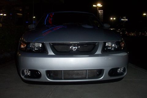 1993 Ford Taurus - Front view of a silver Ford Mustang parked at a dealership at night, with 'TRUCKS' sign visible in the background.