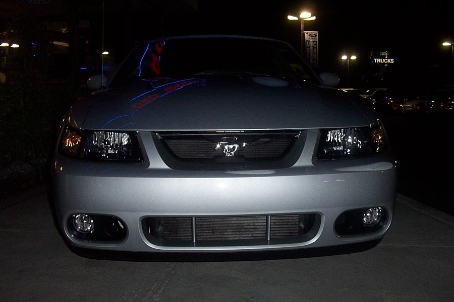 Silver Ford Mustang front view at night. Visible grille emblem, headlights, and lower bumper intake
