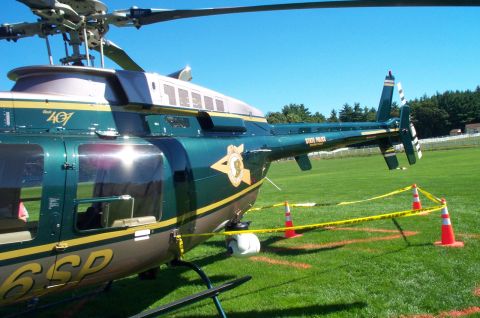 1991 Ford LTD Crown Victoria - A state police helicopter is parked on a grassy field, cordoned off with yellow tape and orange cones.