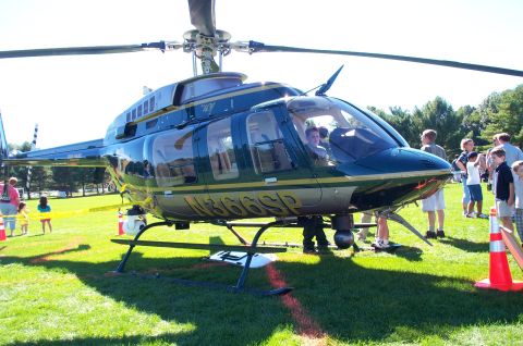 1991 Ford LTD Crown Victoria - A green and gold helicopter with registration N366SP is on display on a grassy field with onlookers.