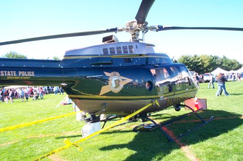 1991 Ford LTD Crown Victoria - A dark green and gold helicopter with 'STATE POLICE' and a badge is parked on a grassy field.