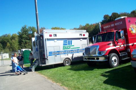 1991 Ford LTD Crown Victoria - Emergency vehicles, including a fire rescue truck and a communications trailer, are parked on grass under a clear blue sky.