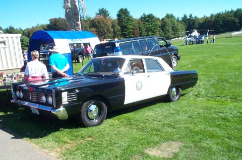1991 Ford LTD Crown Victoria - A vintage police car is on display at an outdoor event with other vehicles and people in the background.