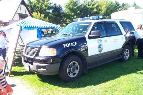 1991 Ford LTD Crown Victoria - A police SUV is parked on a grassy area with tents and trees in the background.