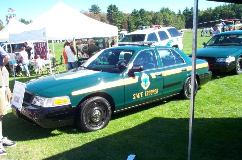 1991 Ford LTD Crown Victoria - Two green state trooper cars are parked on grass with tents and people in the background.