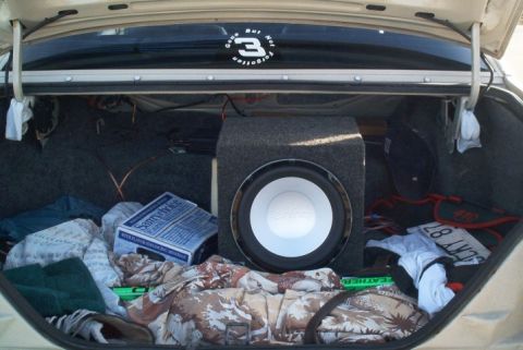 1985 Ford LTD Crown Victoria - The trunk of a car contains a subwoofer, cigarette box, and various personal items.