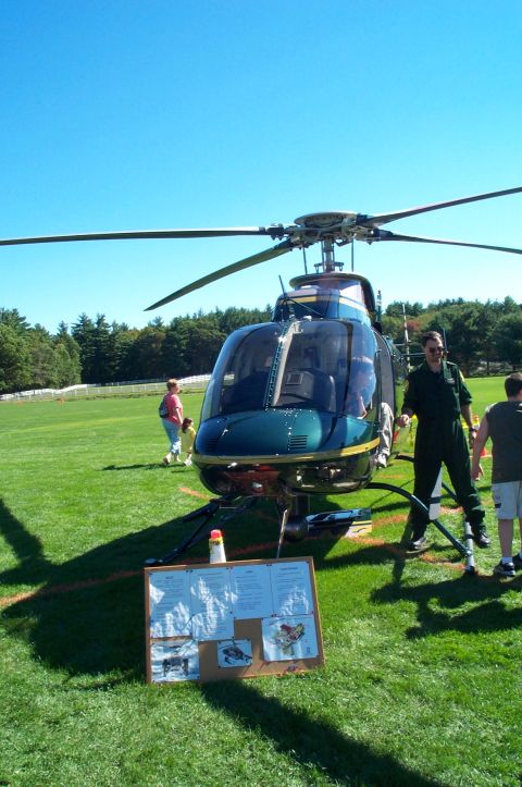 1991 Ford LTD Crown Victoria - A helicopter is parked on a grassy field, with a display board and people nearby.